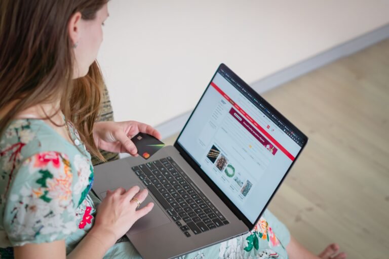 Berapa Biaya Pembuatan Website Bisnis? Panduan Lengkap 2026 Woman in floral dress shopping online with a laptop and credit card indoors.