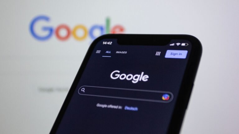 Apakah Bisnis Kecil Perlu Website? Ini Jawabannya Smartphone screen showing Google search in dark mode with the Google logo in the background.
