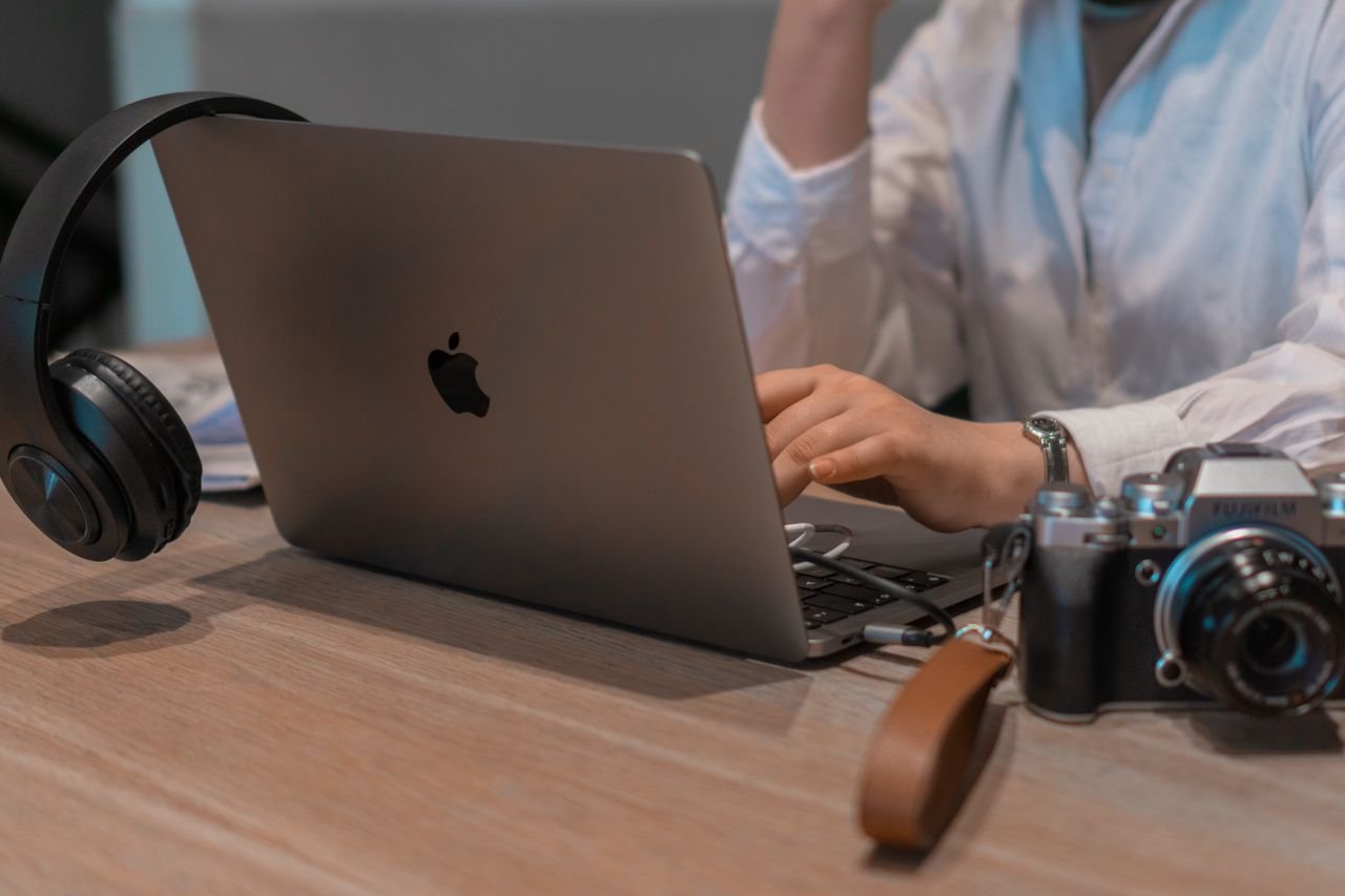 Jasa Pembuatan Website Murah dan SEO-Friendly untuk Bisnis Close-up of a person working remotely with a laptop, headphones, and camera. Ideal for tech and lifestyle themes.